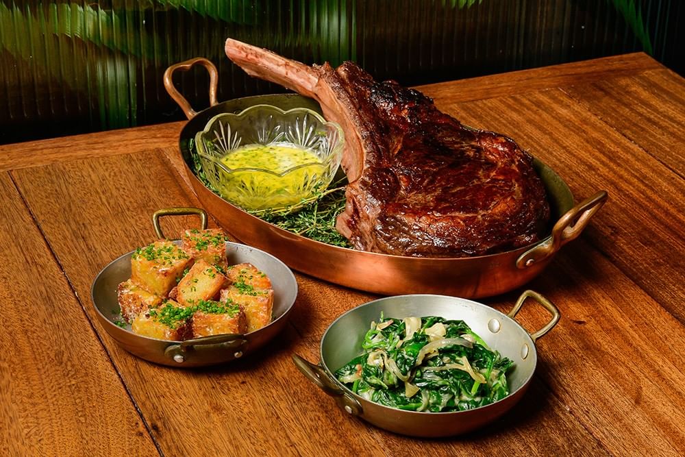 Grilled tomahawk ribeye steak in a copper pan served with roasted potatoes and creamed spinach in Estelle\'s at Gansevoort