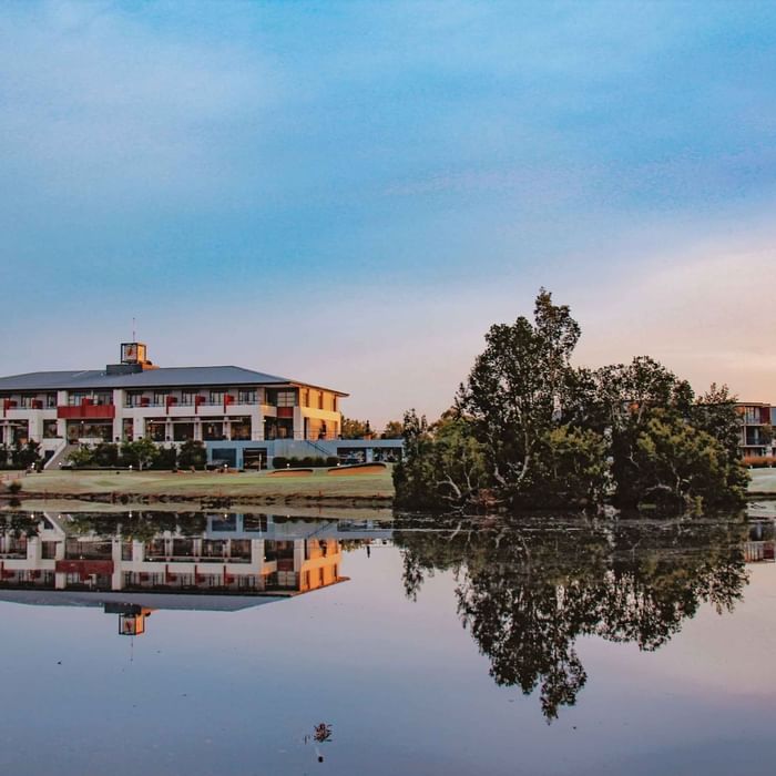 Mercure Kooindah Waters reflected in a calm lake during sunset with trees and a clear sky