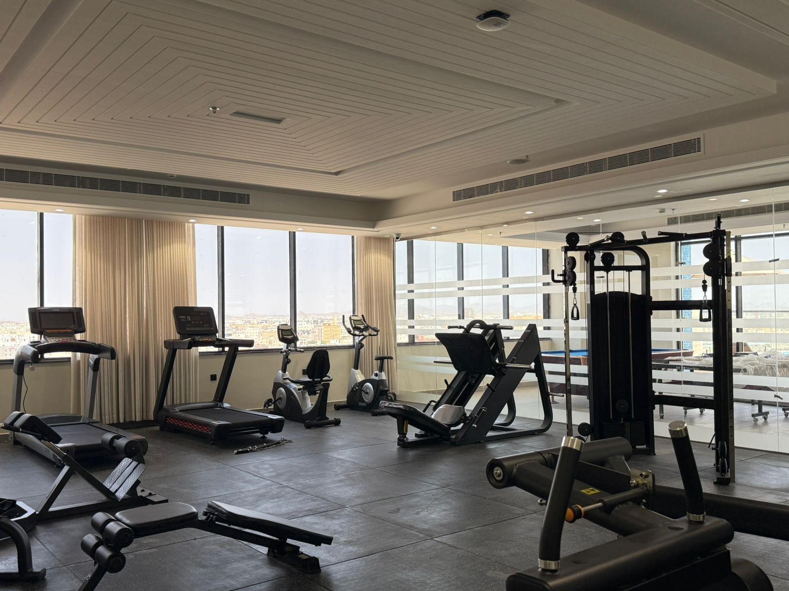 Treadmills by floor-to-ceiling windows under a tiered ceiling in the gym at Warwick Jeddah Hotel & Spa