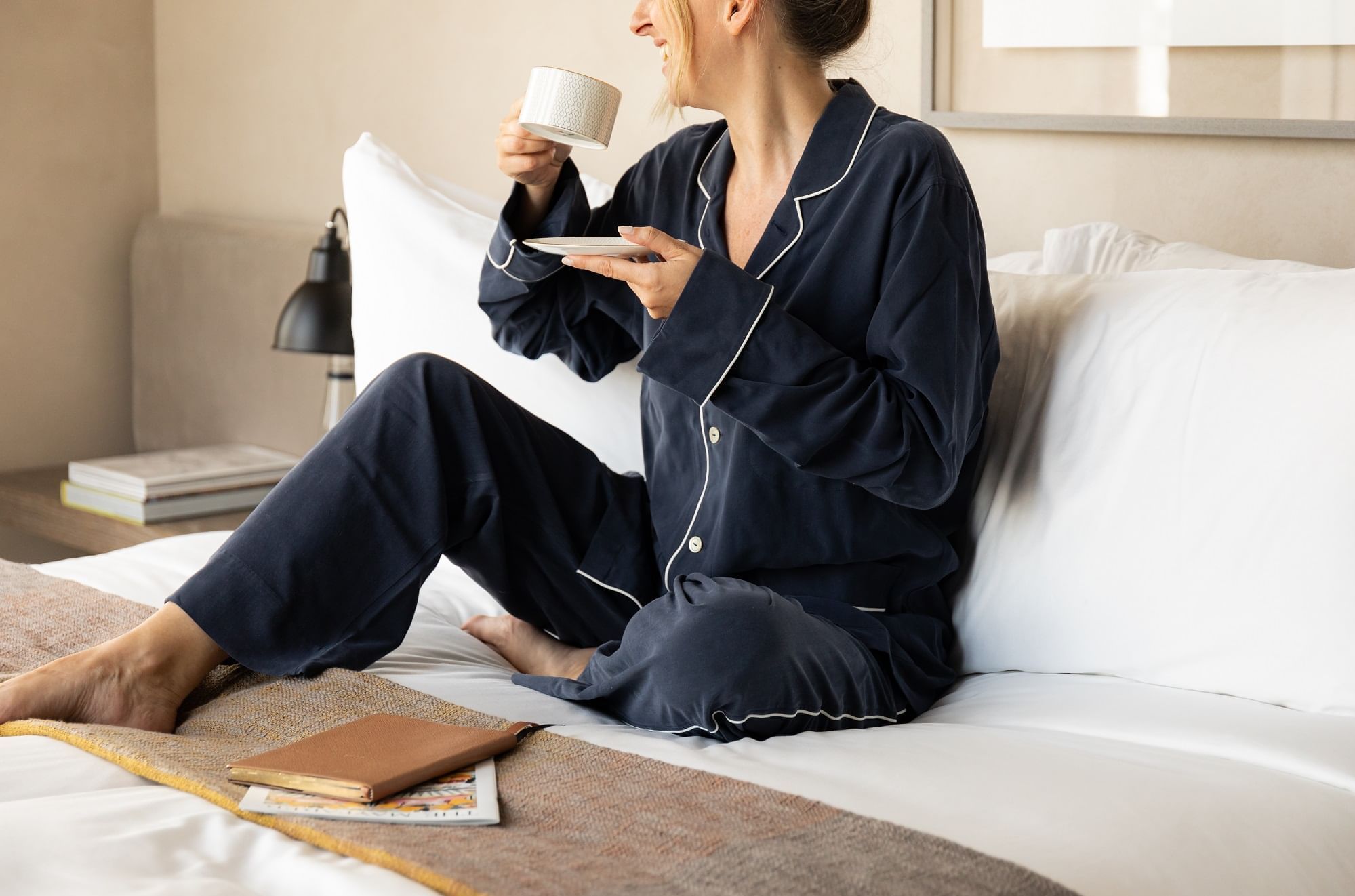 Woman in pajamas comfortably sipping coffee on the comfy bed at The Londoner