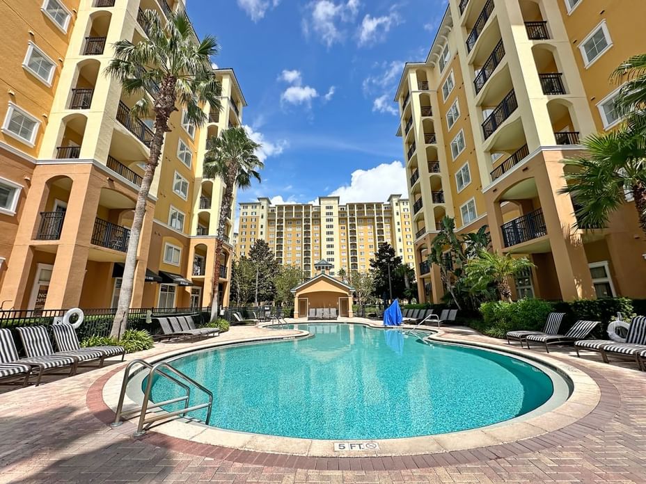 A large pool surrounded by lounge chairs and palm trees, with resort buildings in the background.
