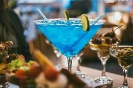Vibrant blue martini cocktail garnished with lime slices and straws beside savory finger foods at Unika Hotels