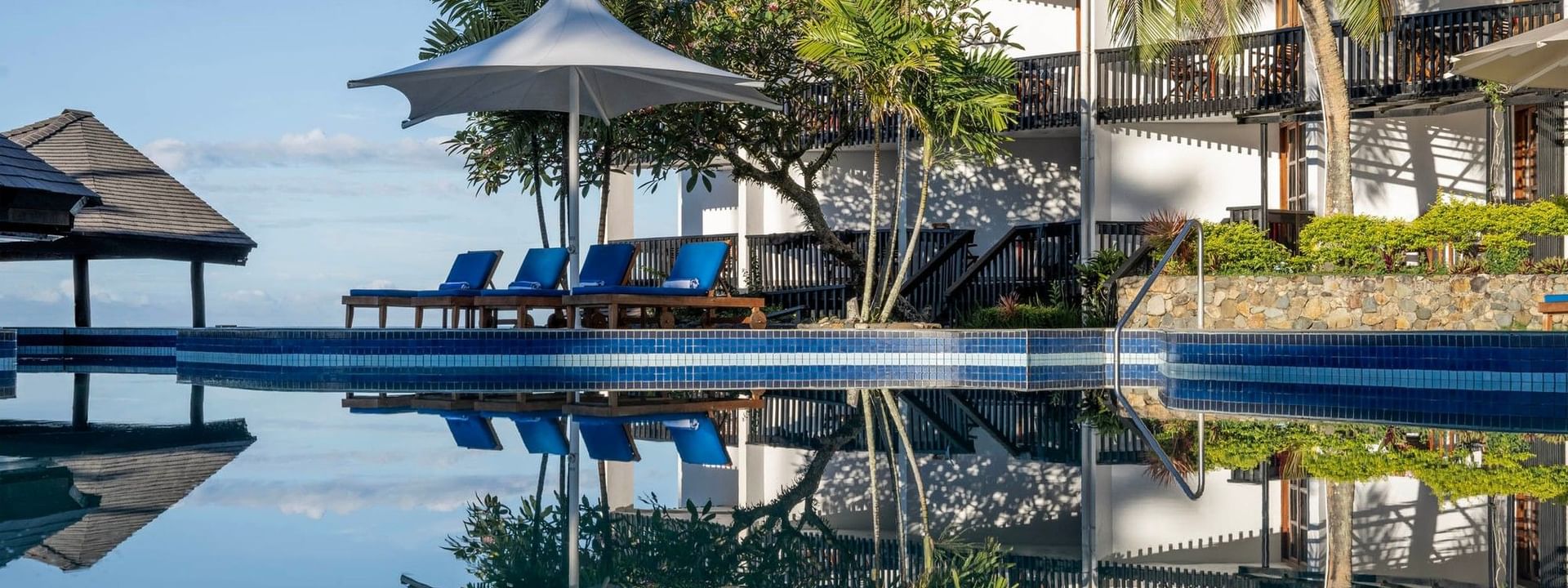 Swimming pool with sun loungers and umbrellas in front of the resort at Warwick Fiji Resort and Spa Korolevu