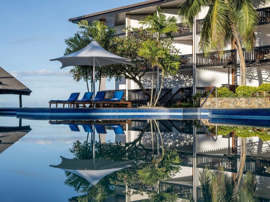 Swimming pool with sun loungers and umbrellas in front of the resort at Warwick Fiji Resort and Spa Korolevu