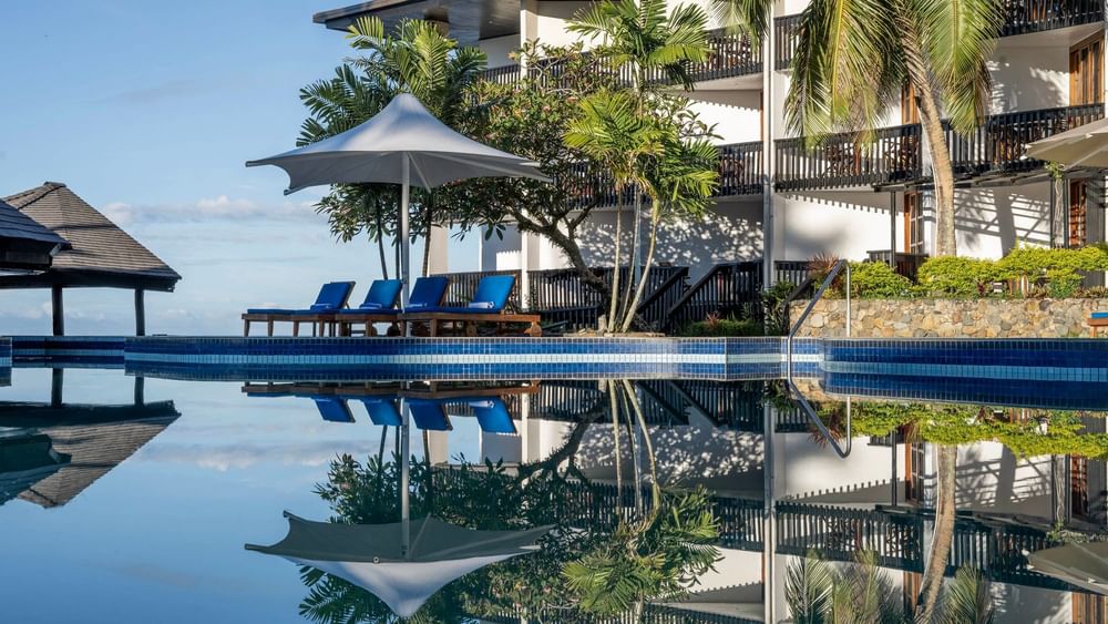Swimming pool with sun loungers and umbrellas in front of the resort at Warwick Fiji Resort and Spa Korolevu.