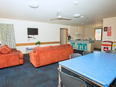 A cozy lounge with orange couches, a blue dining table, and a kitchen area at La Trobe University - Terraces.