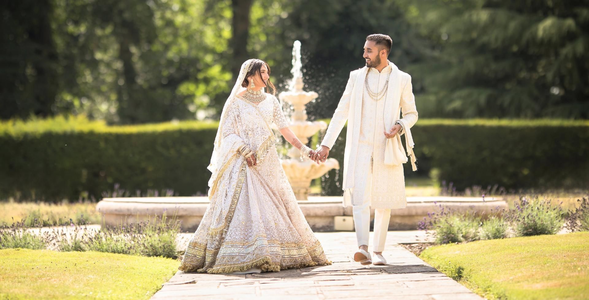 Bride and groom holding hands by fountain at Easthampstead Park, one of the best Asian Wedding Venues in Berkshire
