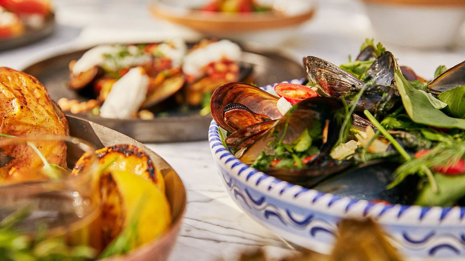 Close-up of steamed mussels in a patterned bowl, with grilled vegetables placed in the background at the Marbella Club