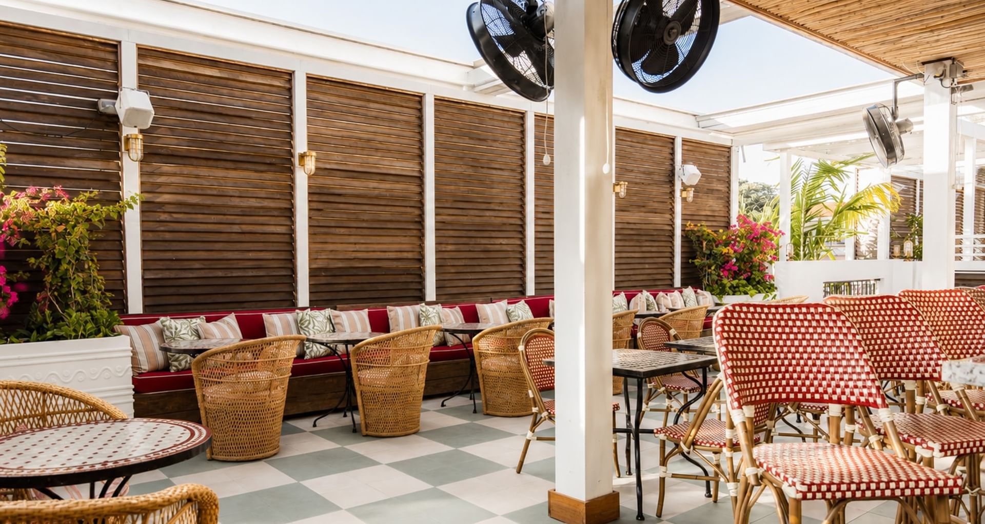 A covered outdoor seating area with red and white checkered chairs, wicker furniture, and decorative pillows.