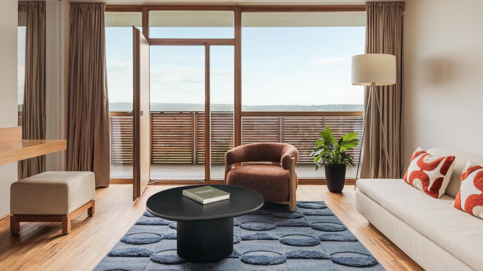 Modern living room with couch, coffee table, chair, potted plant, and balcony overlooking the horizon.