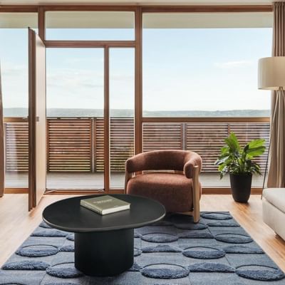 Modernes Wohnzimmer mit Balkon, Möbeln, einem Couchtisch mit Buch und einer Pflanze.