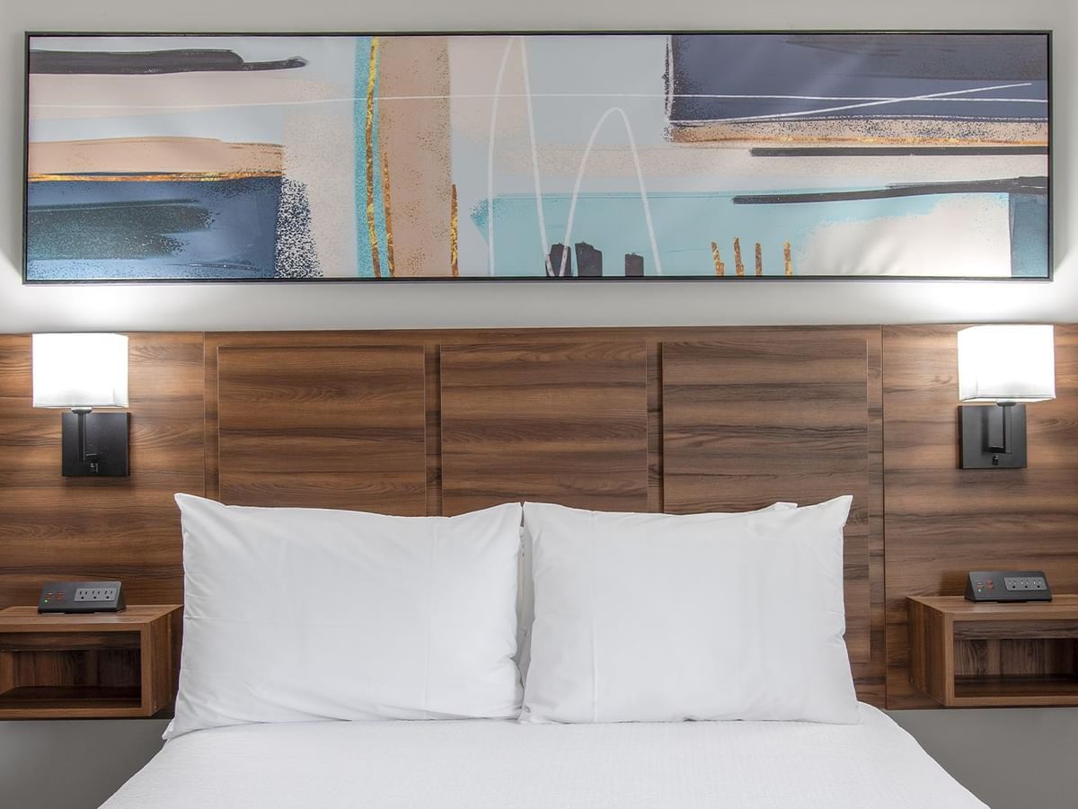 A bed with white pillows and abstract wall art above.