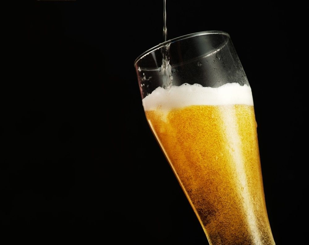 A trickle of beer pouring into a full pint glass of beer against a black background.