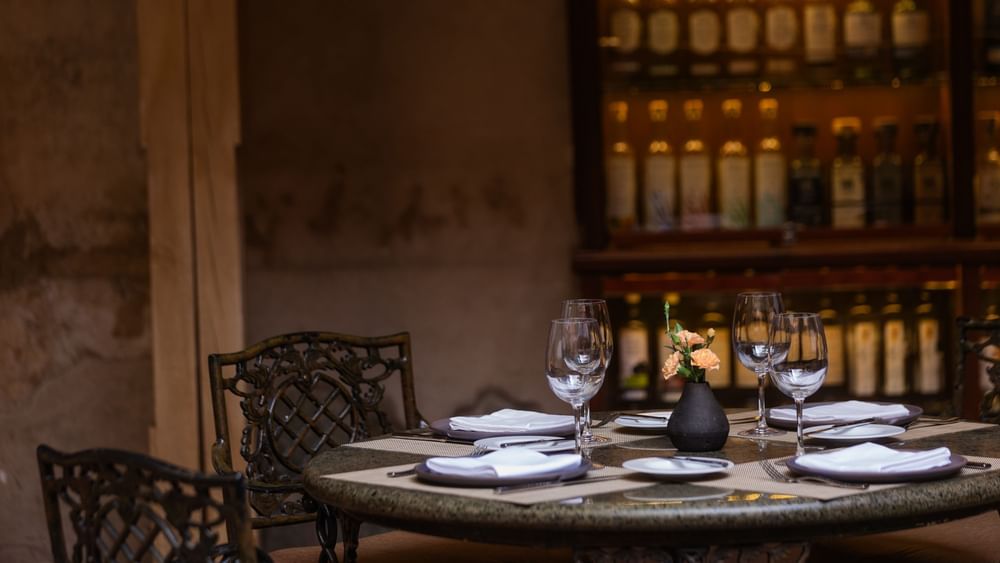 Elegante mesa de restaurante con flores y copas de vino junto a estante de licores en Quinta Real Oaxaca
