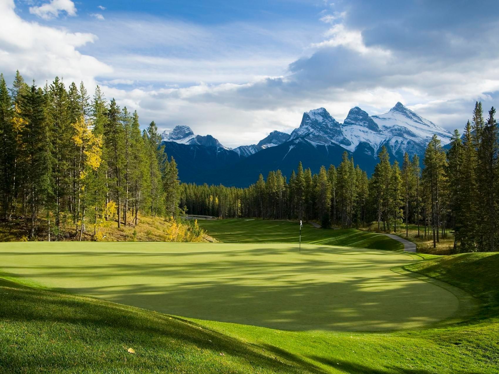 A lush golf course with a flag and mountains in the background near Spring Creek Boardwalk