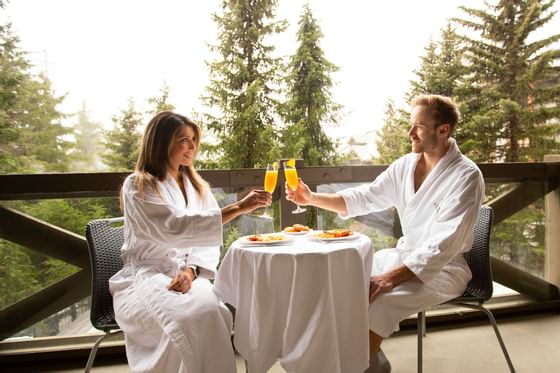 Couple toasting fresh juice in the balcony dining area at Blackcomb Springs Suites