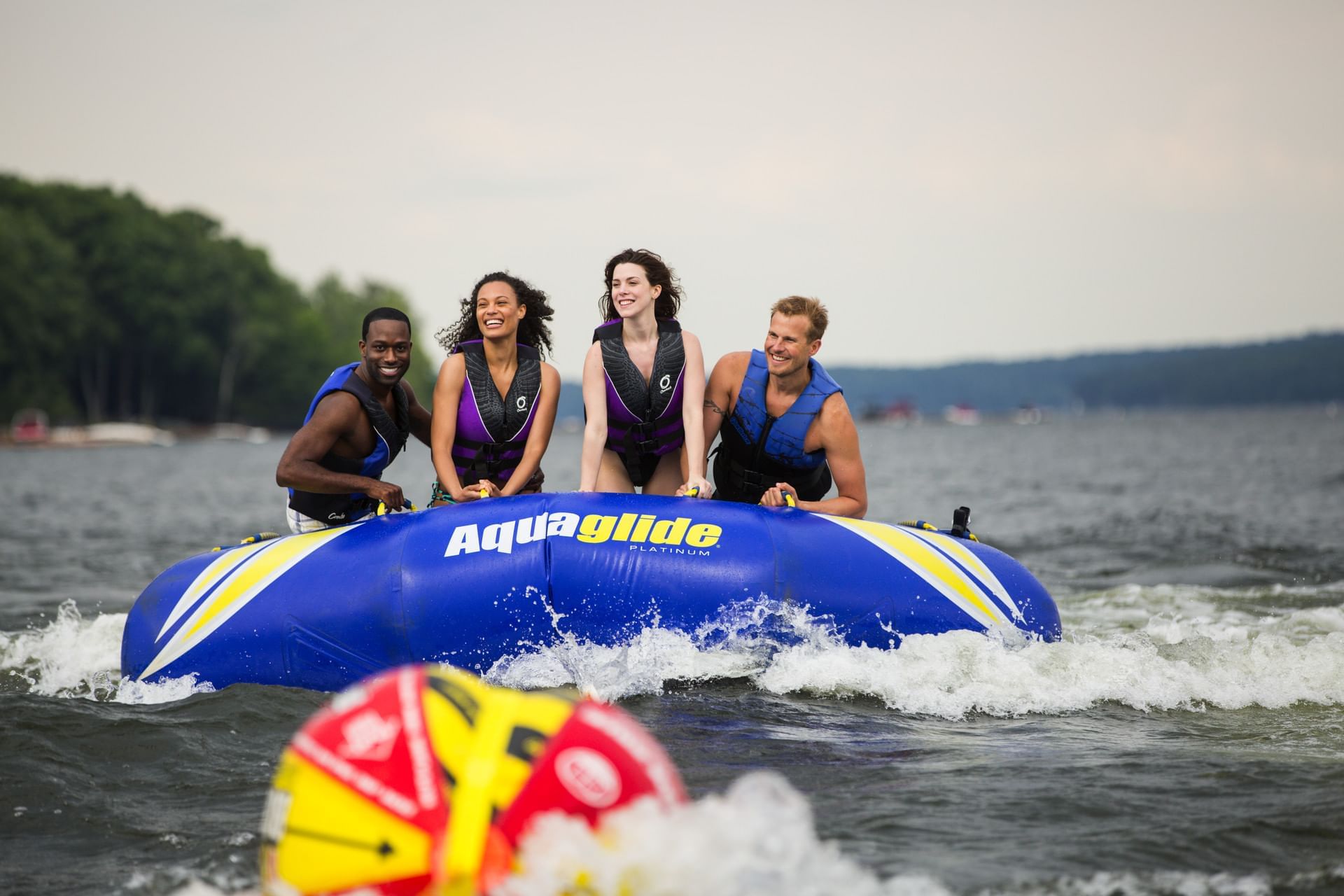 Four people in life vests enjoy tubing on a bright blue inflatable behind a boat near Cove Pocono Resorts