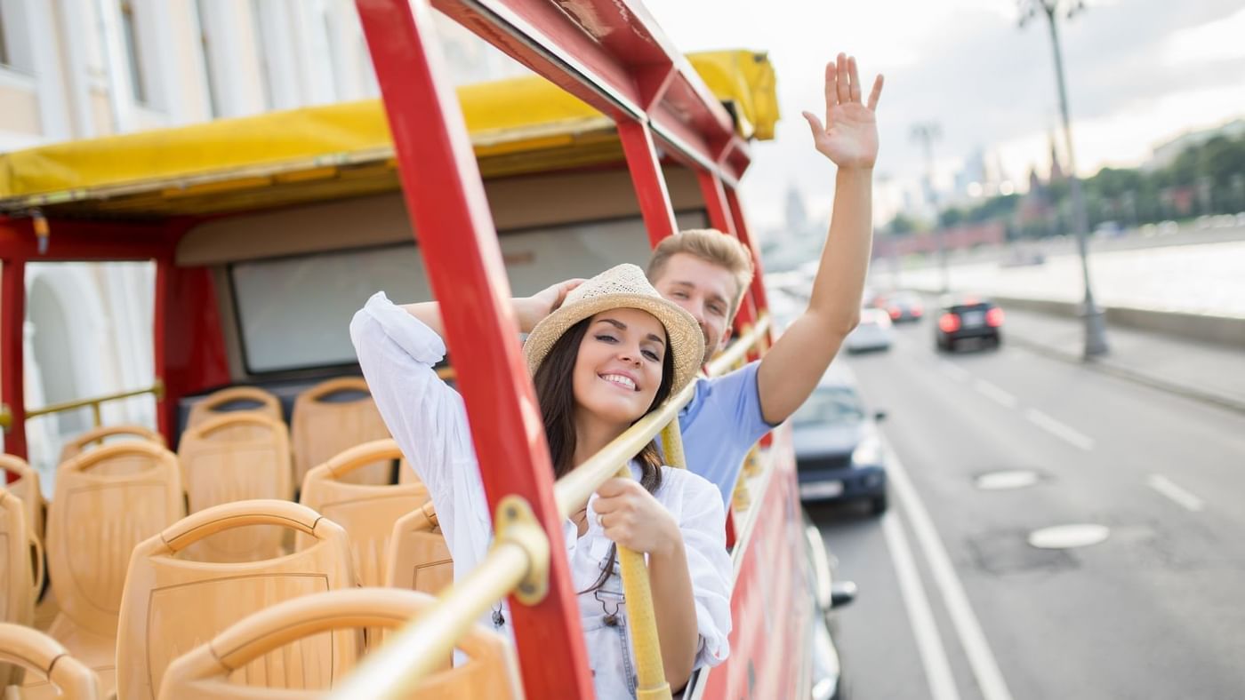 A couple joyfully raises their hands while riding a bus near Grand Fiesta Americana