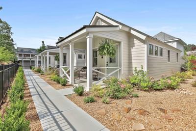 White cottages exterior with porches surrounded by gravel yards and trees under a clear sky, by Cottages at Laurel Brooke