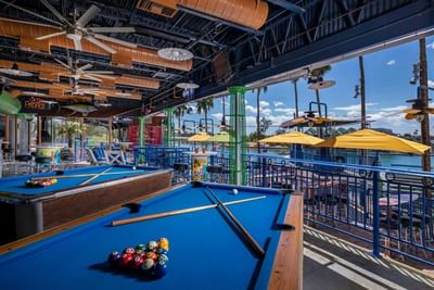 Open-air recreation area with pool tables, yellow umbrellas, and waterfront views at London Bridge Resort