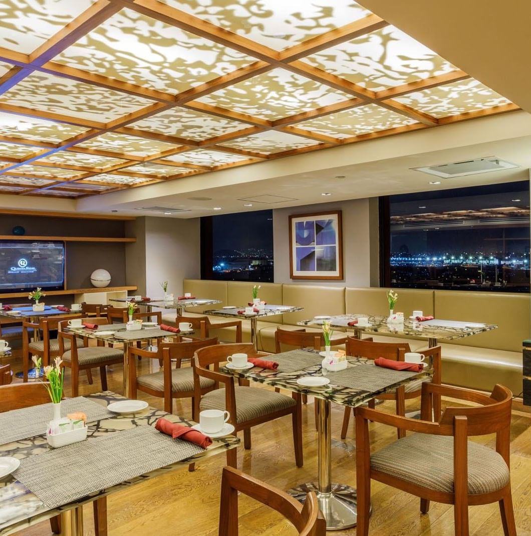Modern dining area featuring wooden tables & chairs by large windows at Camino Real Aeropuerto Mexico