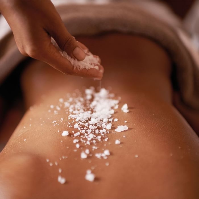 Therapist sprinkling white sea salt crystals on a guests back during a spa treatment at Falkensteiner Hotel & Spa Carinzia