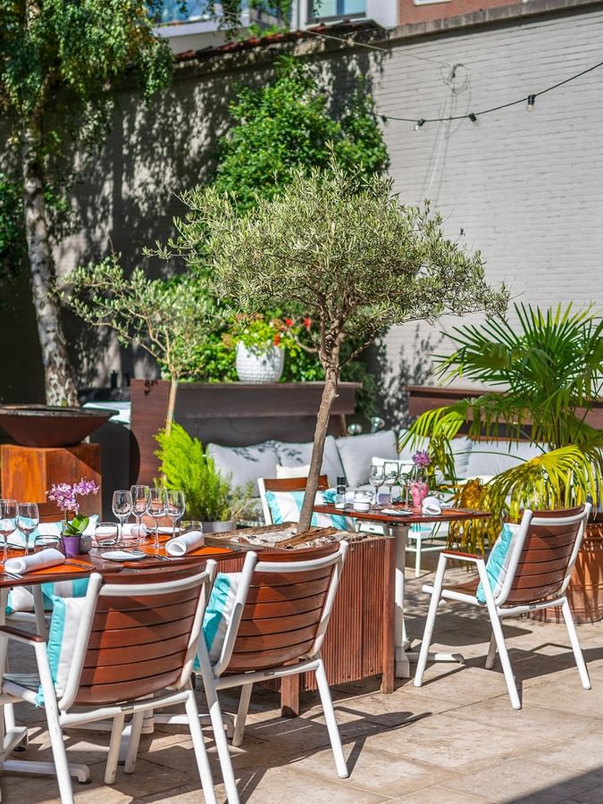 Elegant outdoor terrace dining area with set tables, lush greenery, decorative fountain, and classical statue.
