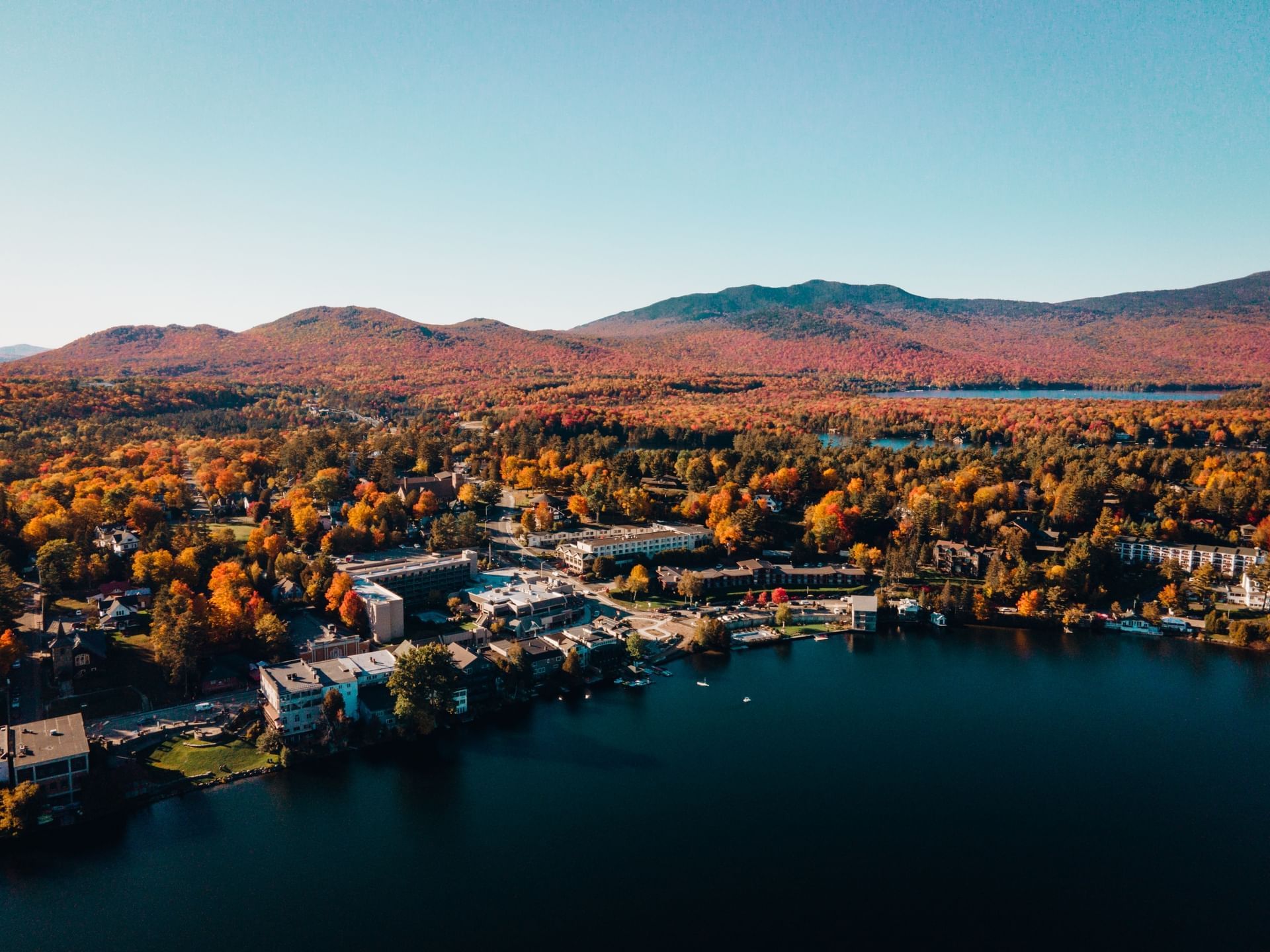 Aerial view of New York State surrounded by vibrant autumn foliage and a Mirror Lake near High Peaks Resort