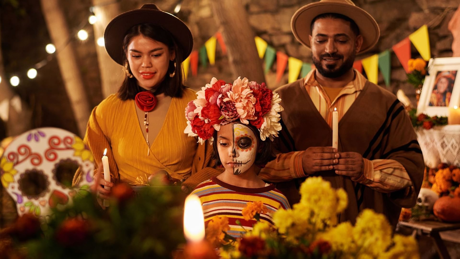 Una familia en Hacienda del Mar Los Cabos celebrando el Día de los Muertos con velas, disfraces y una vibrante corona de flores