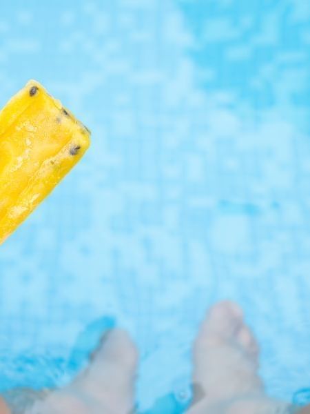 Hand holding a yellow popsicle above clear blue water in PalettAmerica Restaurant at El Conquistador Resort