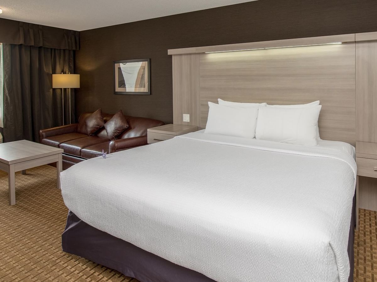 Coast Premium King room with white bedding, brown leather sofa, and city view at Coast Calgary University Area Hotel by APA