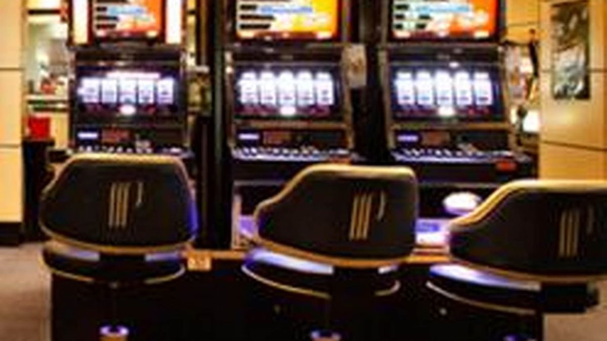 Trois machines à sous alignées avec leurs écrans actifs et trois sièges devant elles.