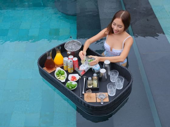A woman is mixing a cocktail at a floating bar in a pool at Peppers Seminyak.