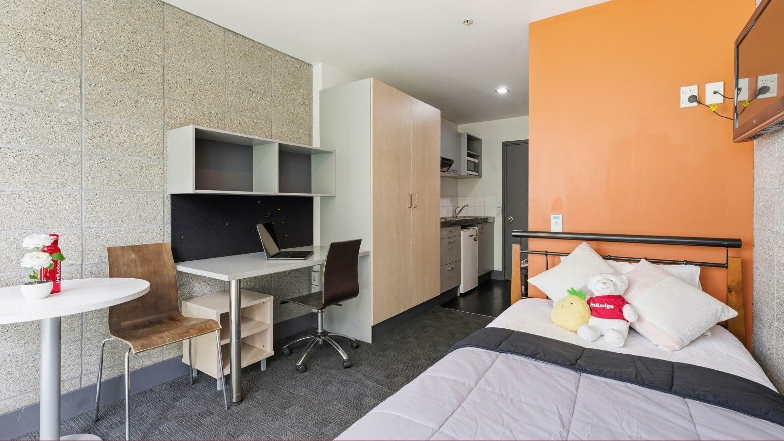 Compact student room with desk, chair, bed, and small kitchen area at Student Living Auckland - Beach.