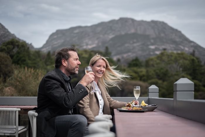 Couple with champagne toasting on a deck overlooking mountains at Freycinet Lodge