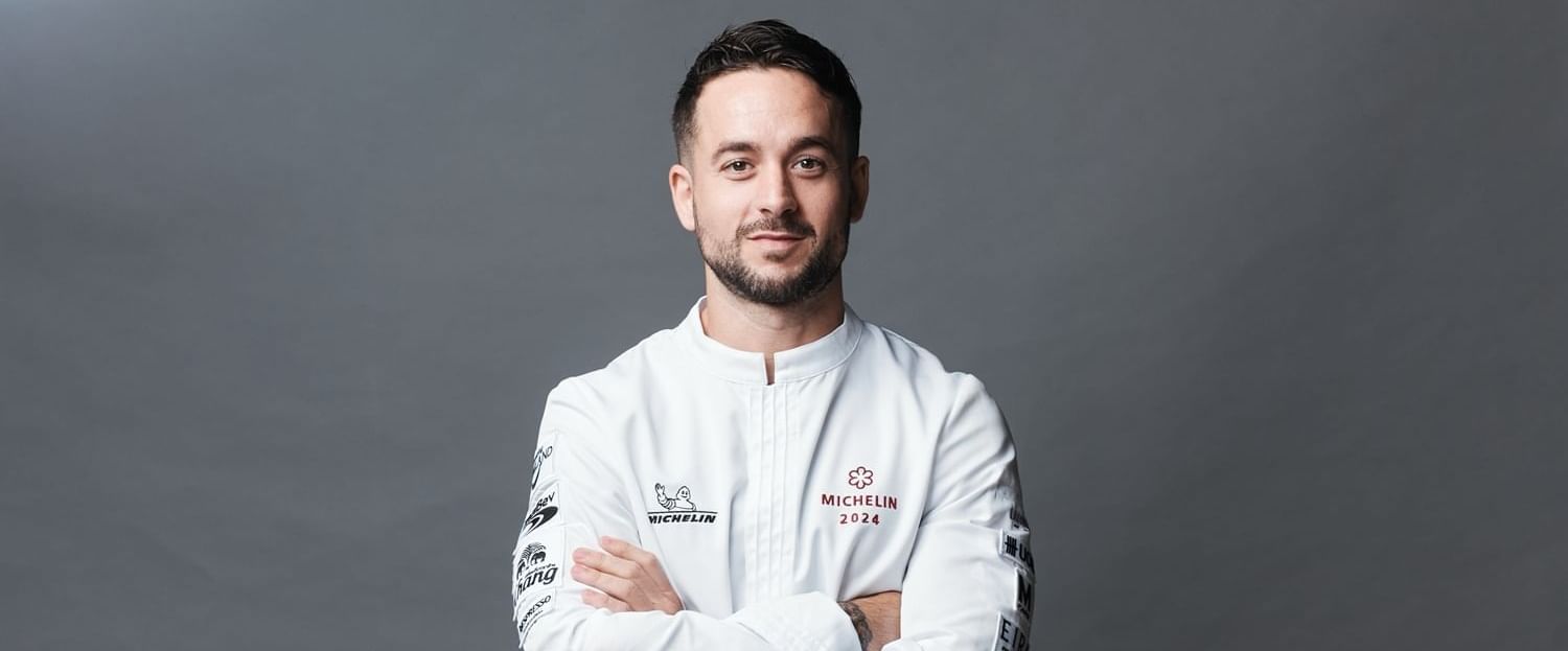 Chef stands confidently with arms crossed against a gray background at The Okura Prestige Bangkok