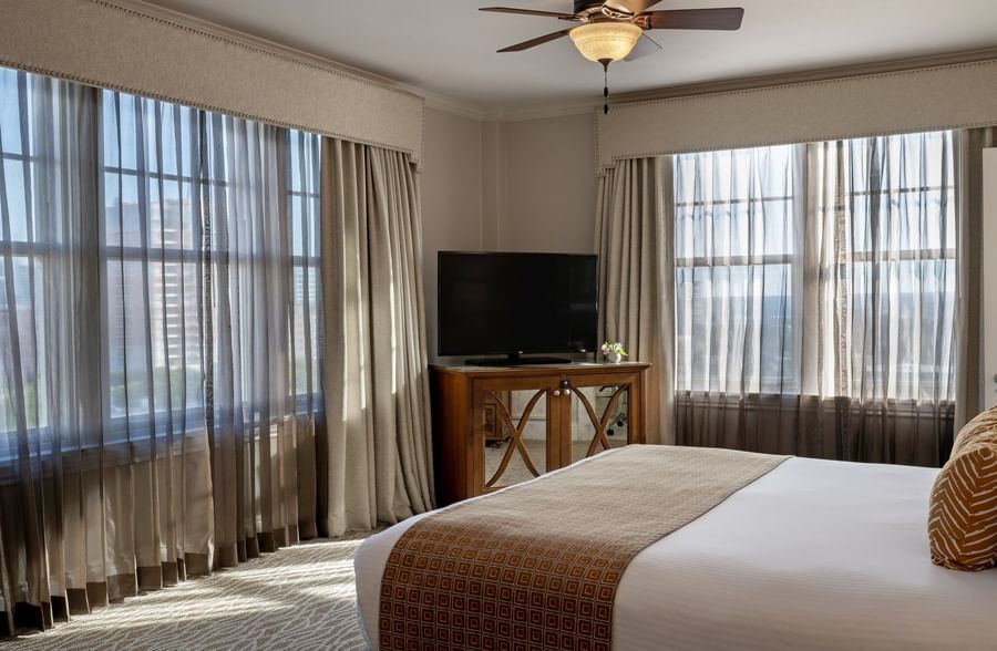 Dark wood TV cabinet by a king bed under a classic brown ceiling fan in Corner King at Warwick Melrose Dallas