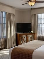 Dark wood TV cabinet by a king bed under a classic brown ceiling fan in Corner King at Warwick Melrose Dallas