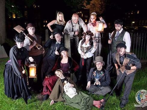 Group of people in Halloween costumes pose for photo in a cemetery at night with lanterns.
