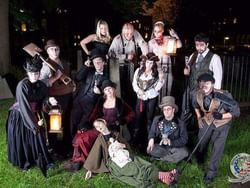 Group of people in Halloween costumes pose for photo in a cemetery at night with lanterns.