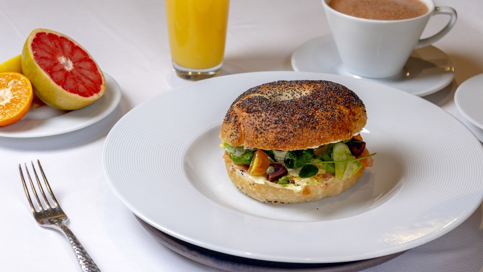 Poppy seed bagel sandwich with greens and tomatoes next to fresh fruit at Quinta Real Oaxaca