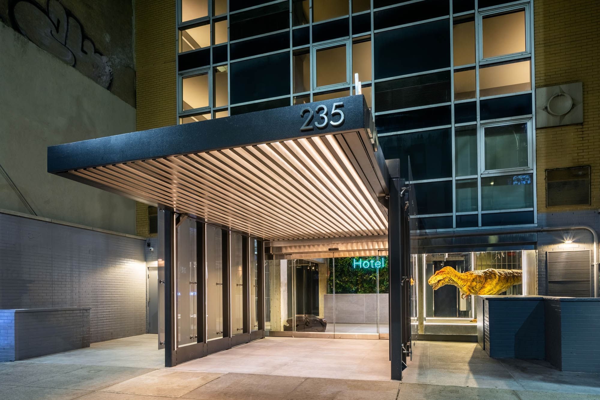 A modern hotel entrance with an awning and glass facade at night.
