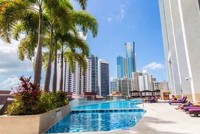 Rooftop pool with palm trees and purple loungers overlooking the Panama City skyline at Megapolis Hotel Panama