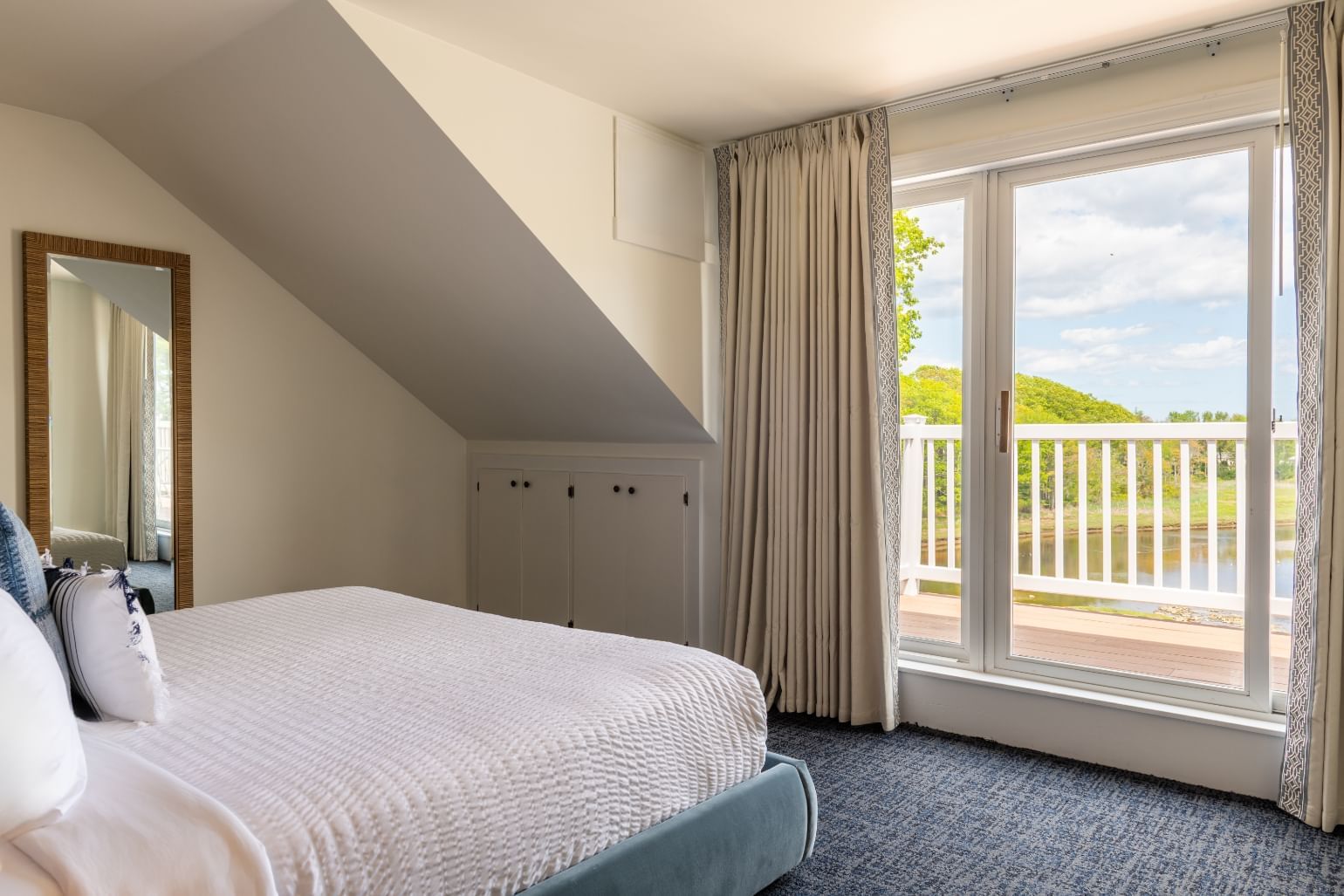 A hotel room with a bed, mirror, and window showing a scenic view.