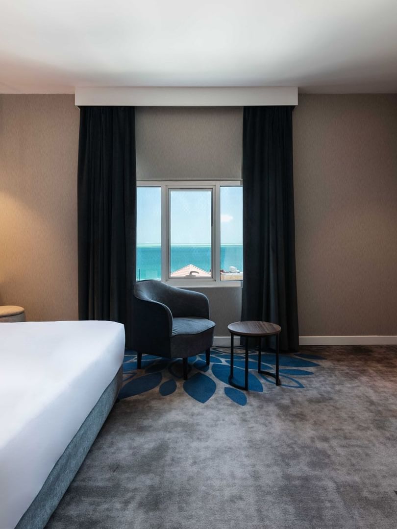 King bed by a grey armchair near a coffee station in Junior Suite Sea View at Warwick Al Jubail