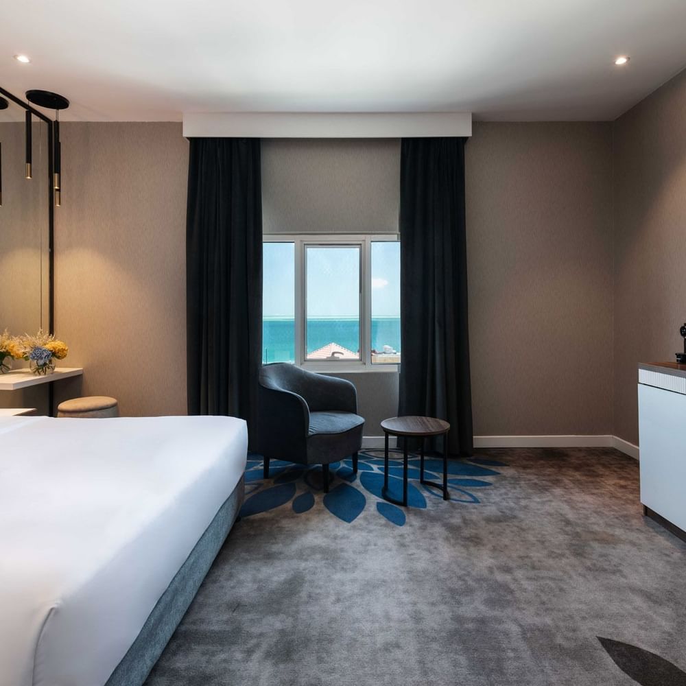 King bed by a grey armchair near a coffee station in Junior Suite Sea View at Warwick Al Jubail