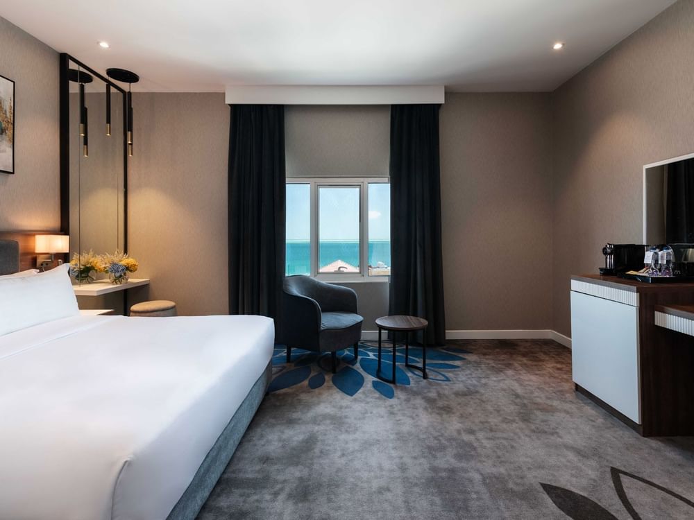 King bed by a grey armchair near a coffee station in Junior Suite Sea View at Warwick Al Jubail