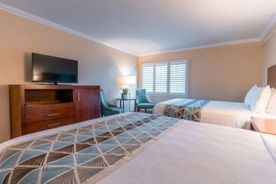 A modern hotel room with two queen beds dressed in white and patterned blue throws at Carmel Bay View Inn