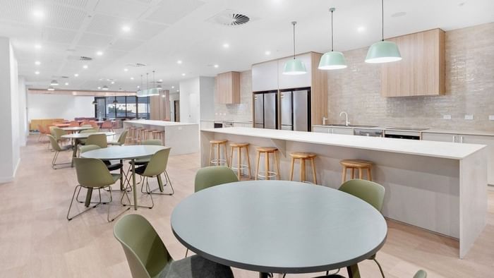 Modern communal kitchen and dining area with white countertops, green stools, and bright lighting at UniLodge Brisbane City.