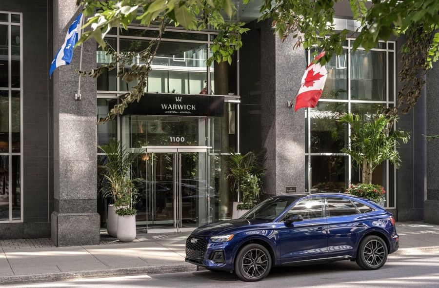 Blue Audi parked by the 1100 entrance glass doors and flags at Warwick Le Crystal Montreal
